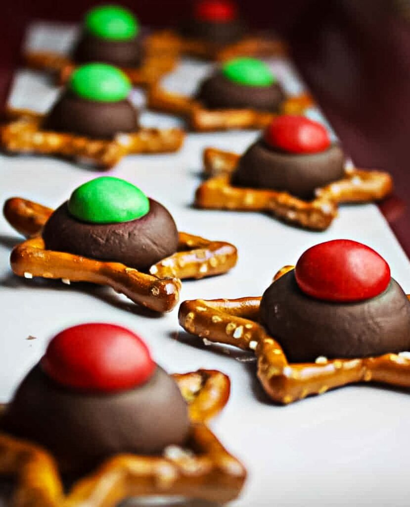 Side view of M&M Pretzel Hugs lined up on a tray, showing melty chocolate and colorful candies on star-shaped pretzels.