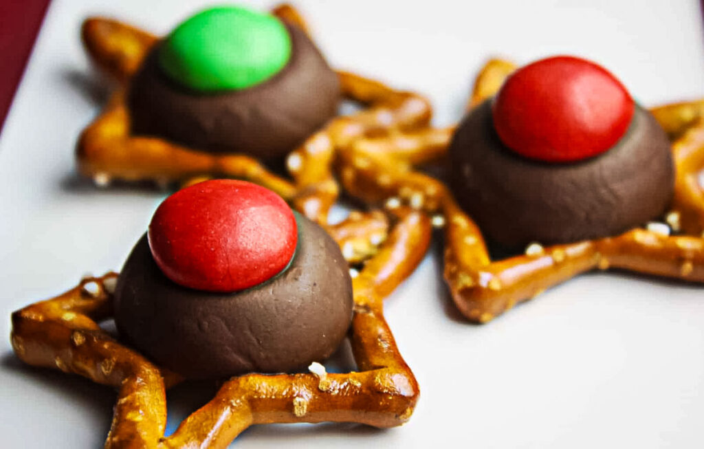 Three M&M Pretzel Hugs arranged on a white platter, each made with a chocolate kiss and a festive red or green candy.