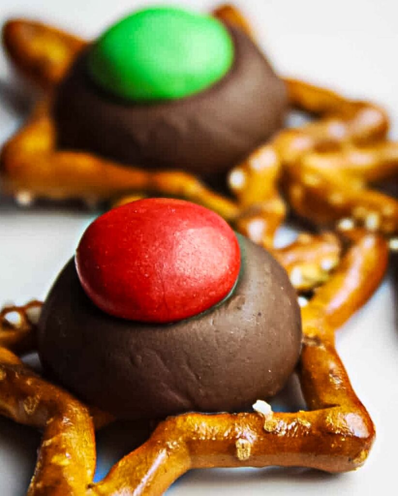 Close-up of a star-shaped pretzel topped with a melted Hershey's Kiss and a red holiday M&M.
