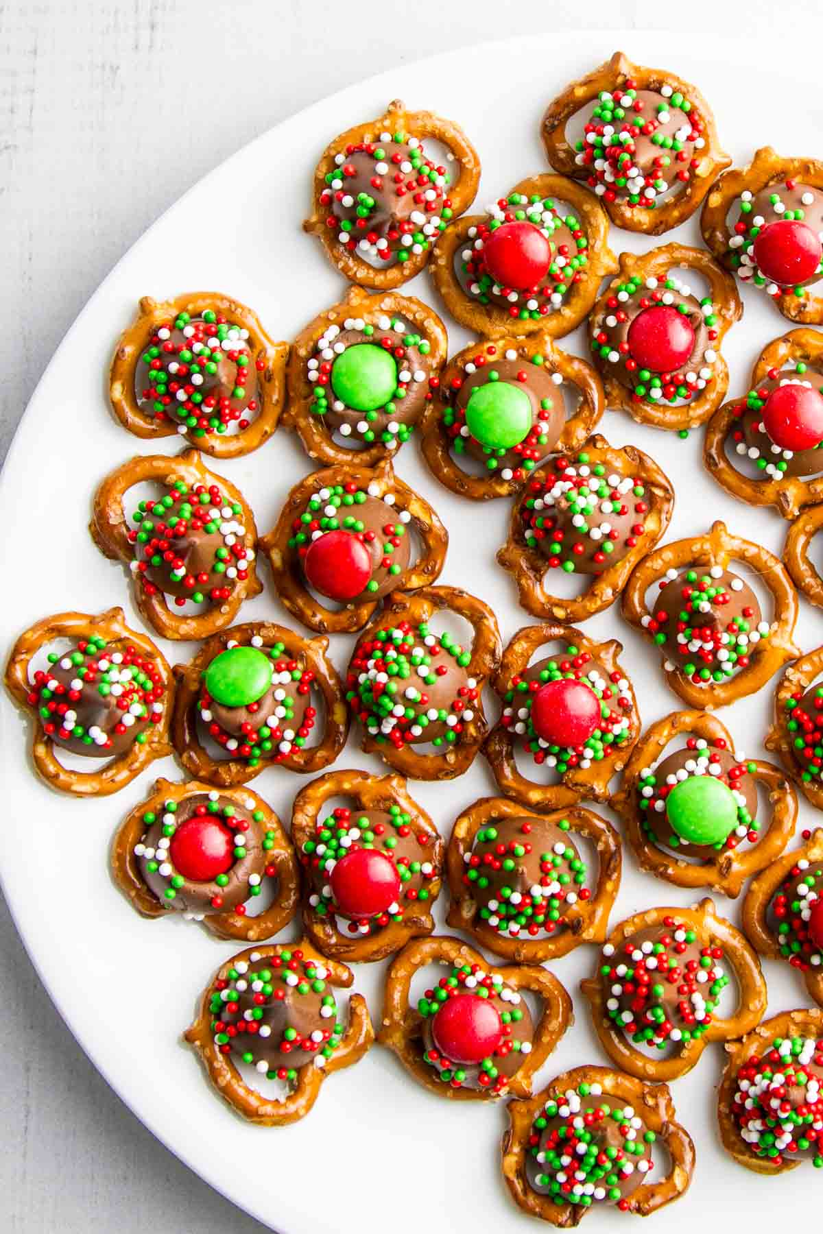 a cookie plate filled with christmas m&m pretzel hugs with sprinkles
