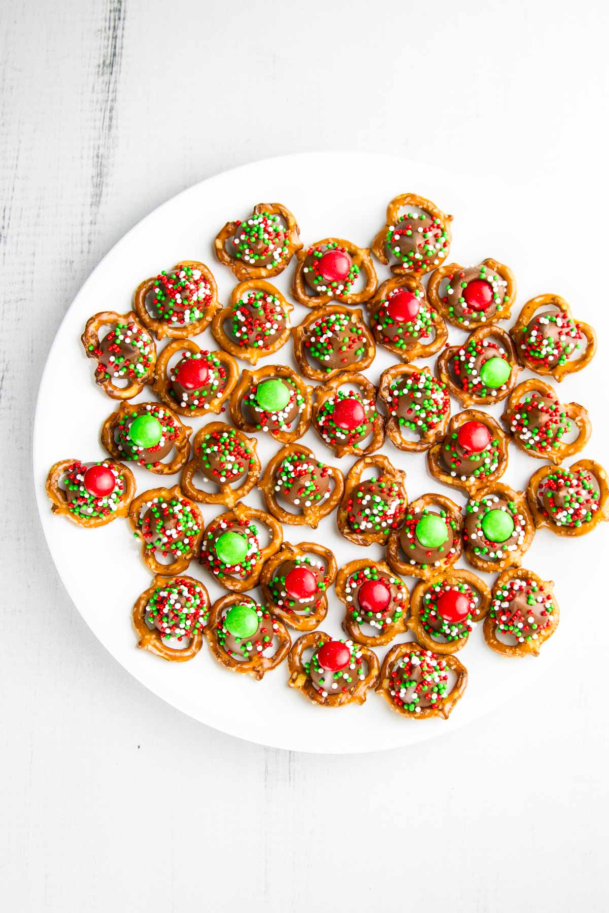 a white cookie plate filled with christmas m&m pretzel hugs with sprinkles