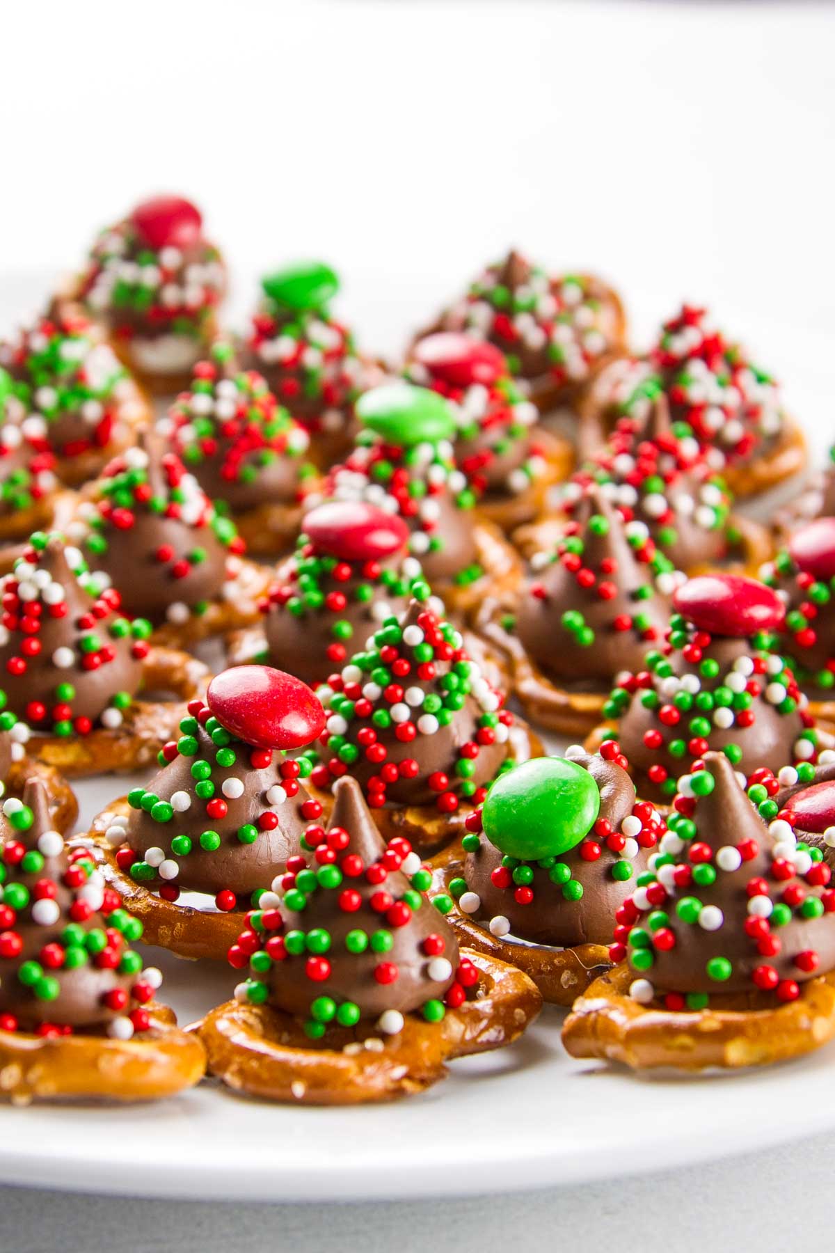 a side view of a white cookie plate filled with christmas m&m pretzel hugs with sprinkles