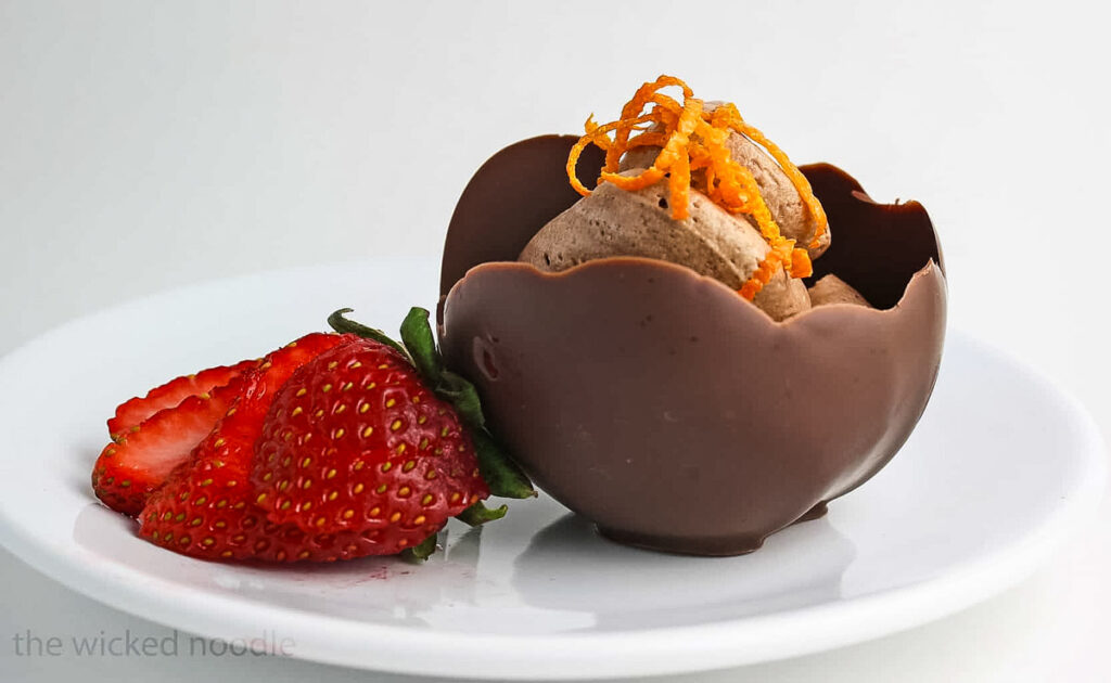 Easy Chocolate Bowls with Balloons – A Fun No-Bake Dessert! Chocolate bowl filled with mousse, garnished with orange zest and fresh strawberries on a white plate