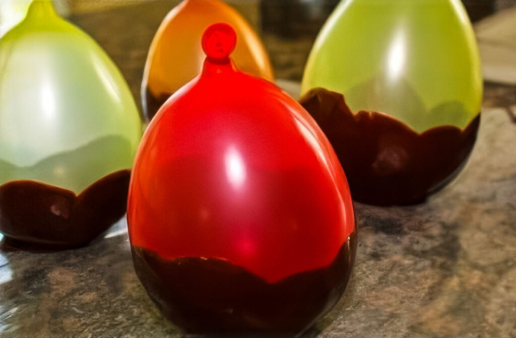 Easy Chocolate Bowls with Balloons – A Fun No-Bake Dessert! Colorful balloons coated in chocolate bottoms, drying on a stone countertop to make chocolate bowls with balloons
