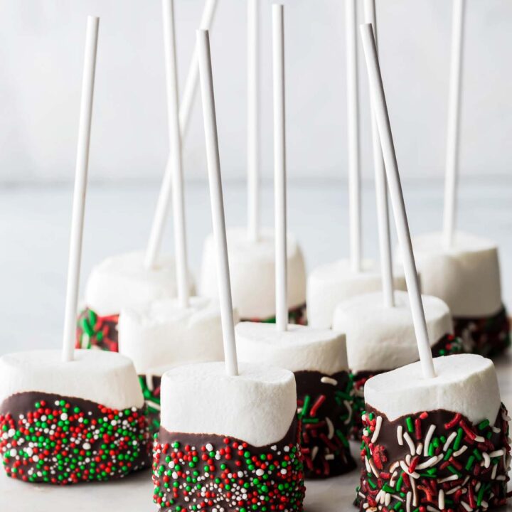 A row of marshmallow pops coated in chocolate and festive sprinkles resting on parchment paper