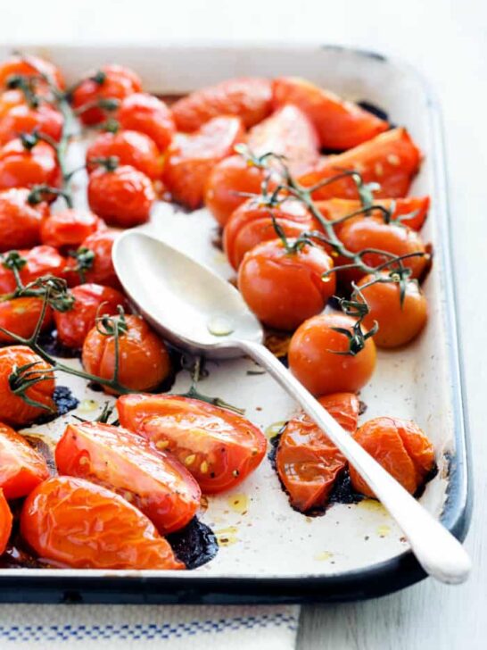 Baking tray filled with delicious juicy oven roasted tomatoes with large serving spoon