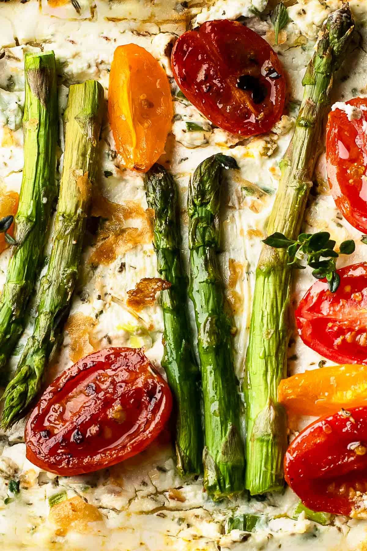 Asparagus Goat Cheese Tart a closeup of an asparagus goat cheese tart with halved cherry tomatoes and fresh herbs