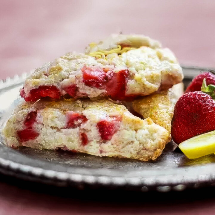 a vintage plate holds three strawberry lemon scones and a few fresh strawberries and lemon slices