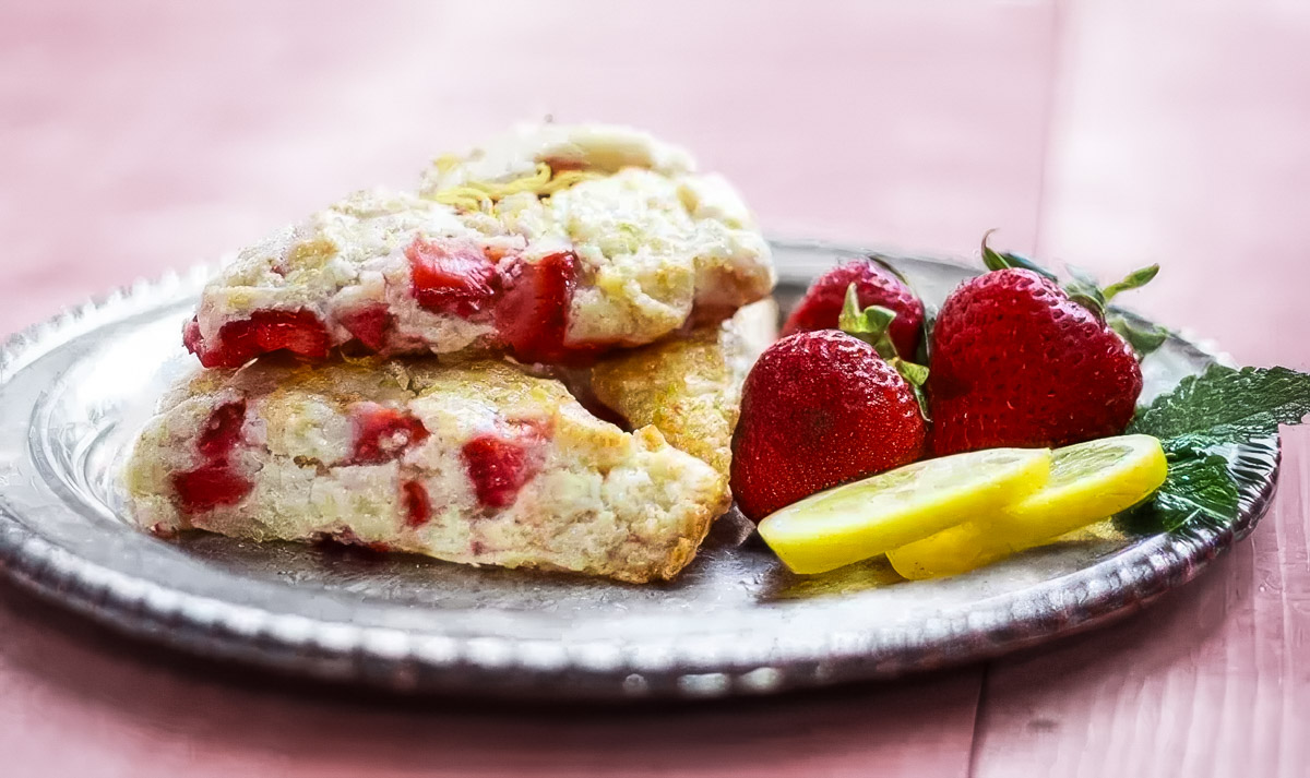 Strawberry Lemon Scones a vintage plate holds three strawberry lemon scones and a few fresh strawberries and lemon slices