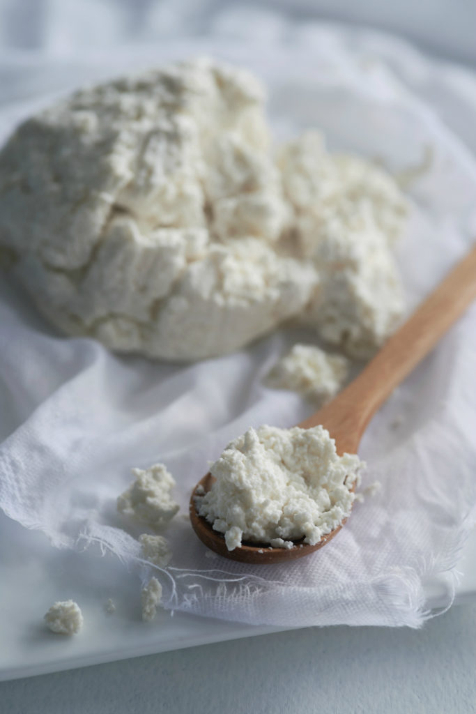 Spoonful of fresh homemade ricotta cottage cheese made from milk, draining on muslin cloth