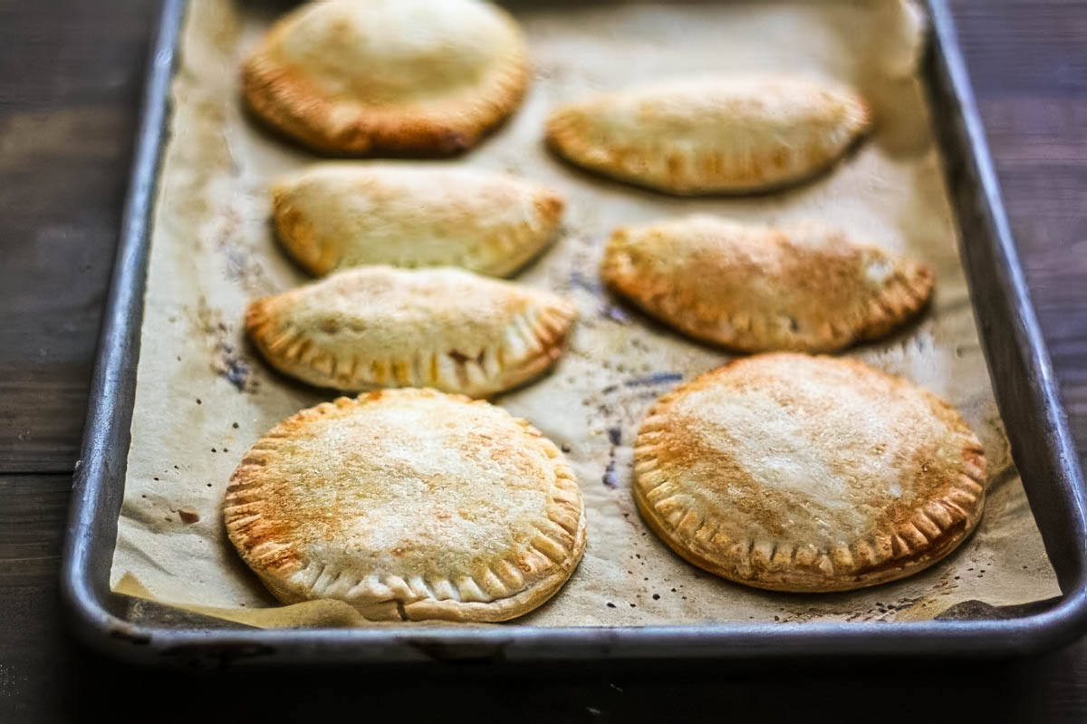 The Best Peach Hand Pies – Simple Summer Dessert peach hand pies just out of the oven, on a parchment lined sheet pan