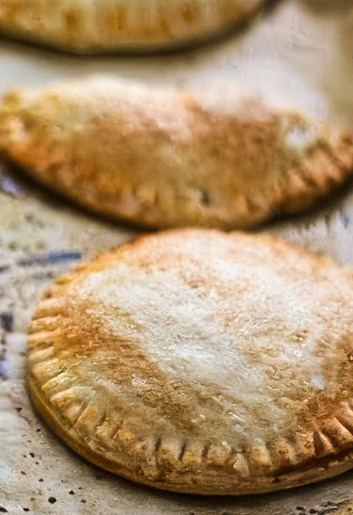The Best Peach Hand Pies – Simple Summer Dessert two peach hand pies just out of the oven, on a parchment lined sheet pan