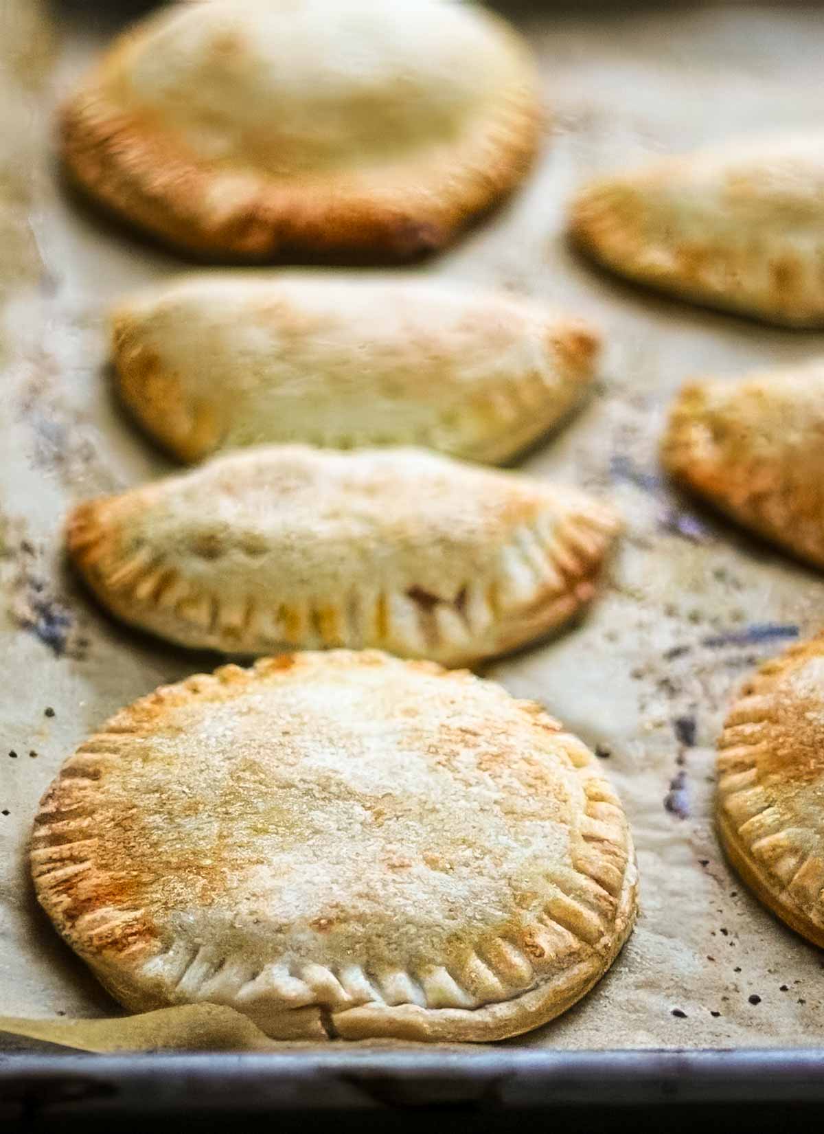 The Best Peach Hand Pies – Simple Summer Dessert a closeup of peach hand pies just out of the oven, on a parchment lined sheet pan