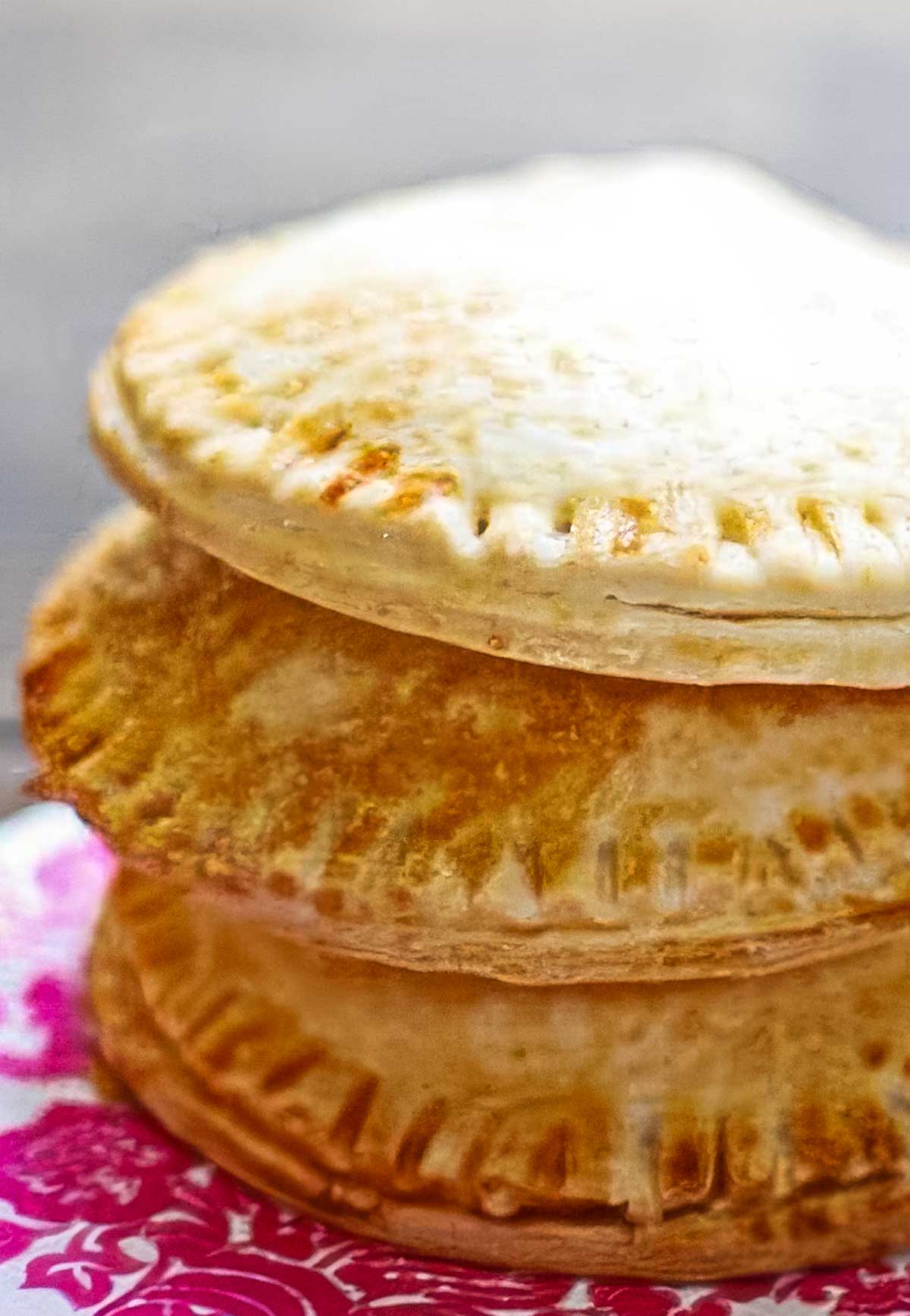 The Best Peach Hand Pies – Simple Summer Dessert a stack of three peach hand pies on a pink and white decorative napkin