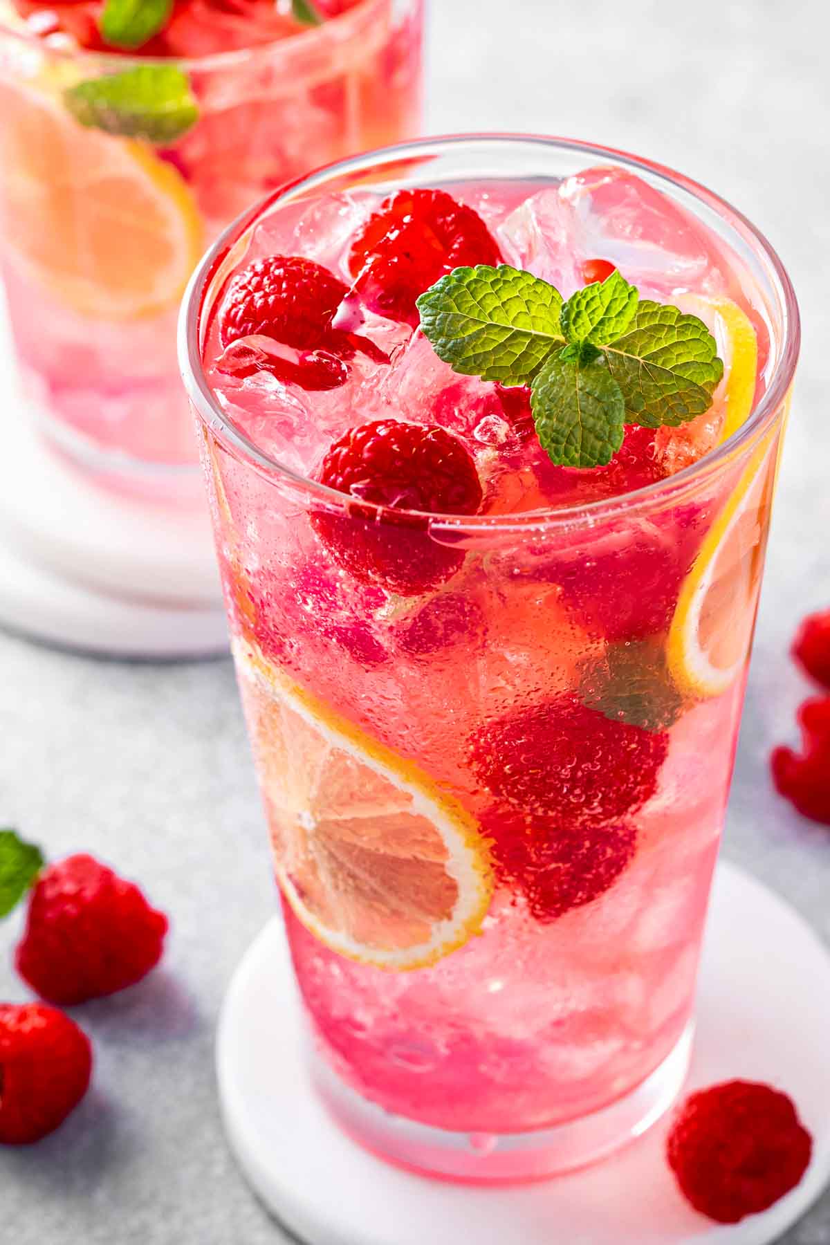 a closeup of a glass of raspberry lemonade with thin lemon slices, fresh raspberries, and a sprig of fresh mint