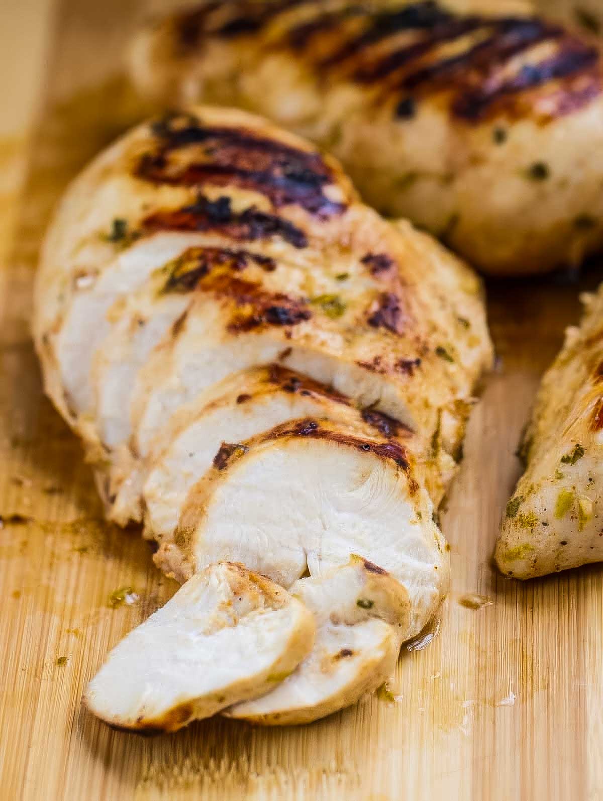 a cilantro lime chicken breast with visible grill marks resting on a wooden cutting board after just having been sliced