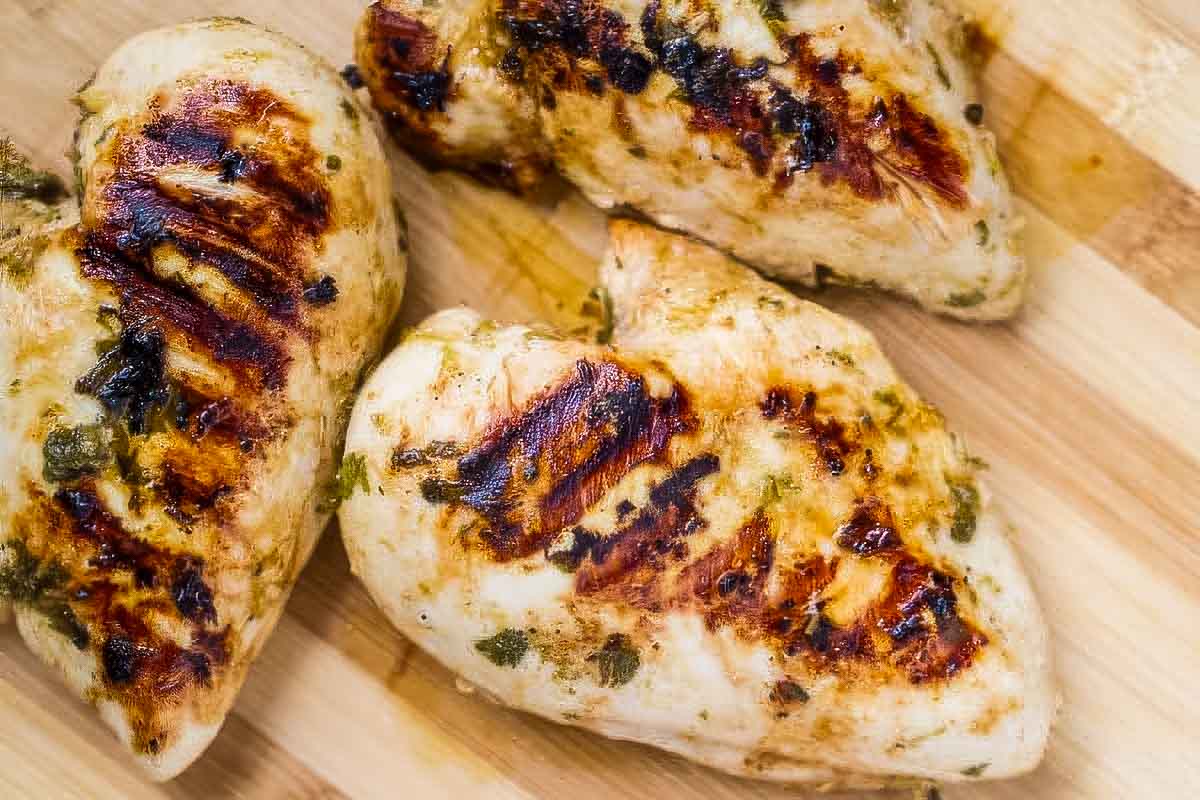 Cilantro Lime Chicken (Grilled, Baked, or Air Fried!) three cilantro lime chicken breasts with visible grill marks resting on a wooden cutting board