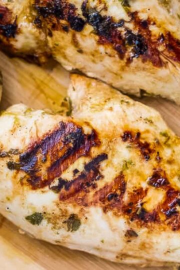 a closeup of three cilantro lime chicken breasts with visible grill marks resting on a wooden cutting board