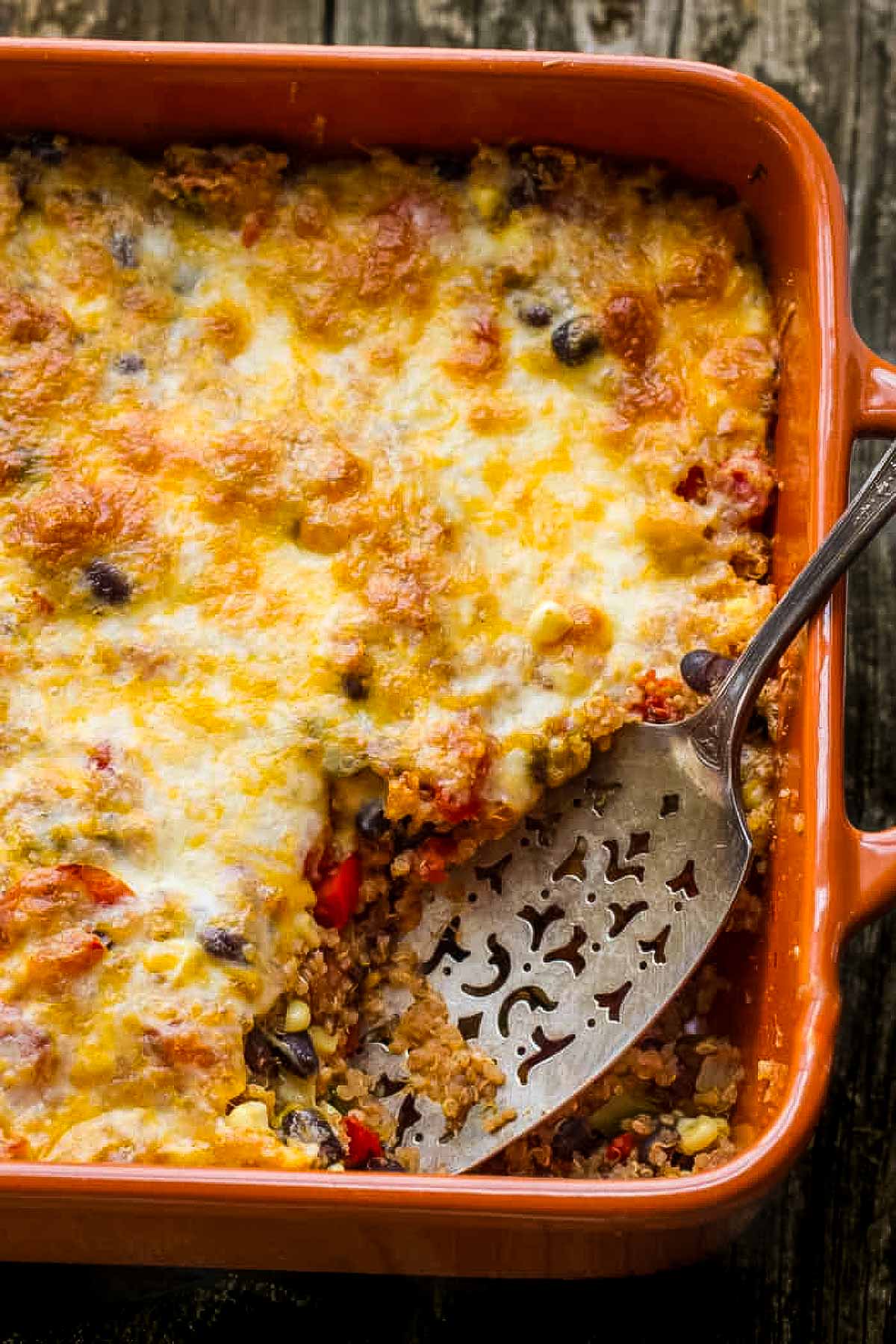 Healthy Mexican Quinoa Casserole a Mexican quinoa casserole just out of the oven on a rustic wood table with a vintage spatula taking out the first serving