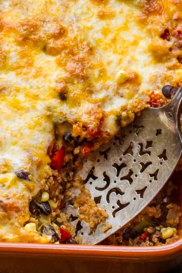 Healthy Mexican Quinoa Casserole a closeup of a Mexican quinoa casserole just out of the oven on a rustic wood table with a vintage spatula taking out the first serving