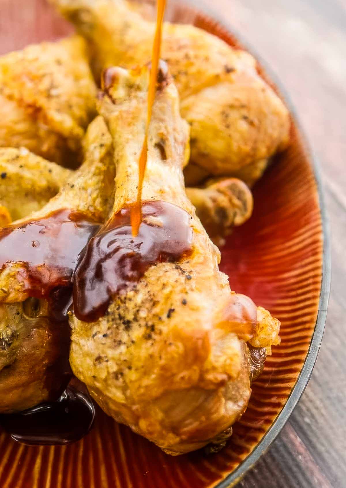 Easy Baked Chicken Drumsticks with Garlic-Honey Asian Glaze baked chicken drumsticks just out of the oven being drizzled with a delicious asian sauce