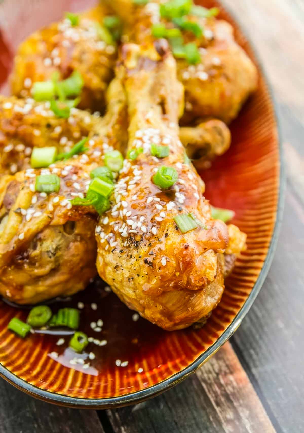 Easy Baked Chicken Drumsticks with Garlic-Honey Asian Glaze baked chicken drumsticks just out of the oven, topped with a delicious asian sauce, chopped green onions, and sesame seeds
