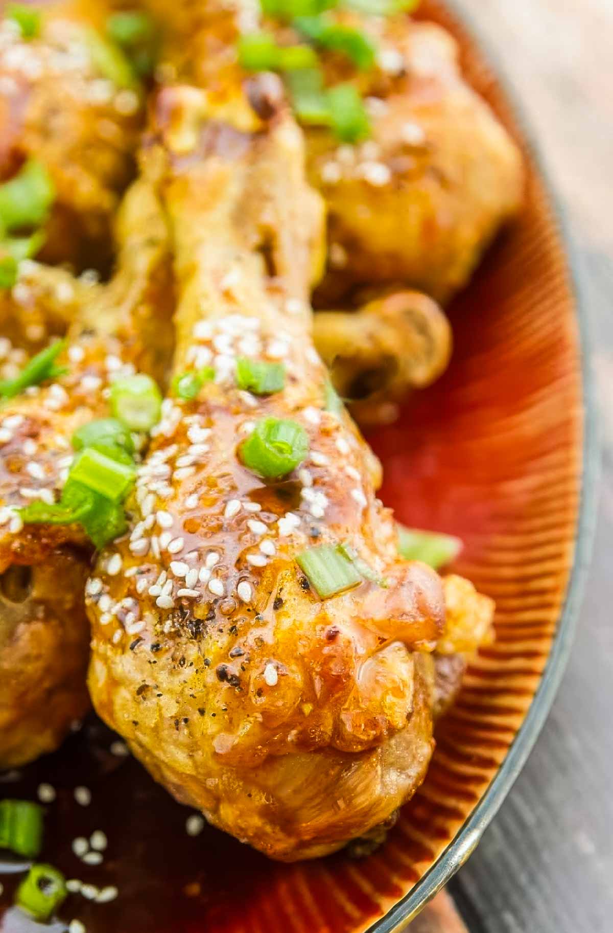Easy Baked Chicken Drumsticks with Garlic-Honey Asian Glaze a closeup of baked chicken drumsticks just out of the oven, topped with a delicious asian sauce, chopped green onions, and sesame seeds