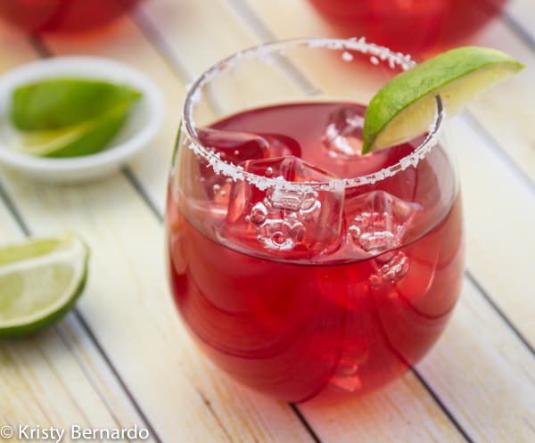 A pomegranate margarita with a wedge of fresh lime