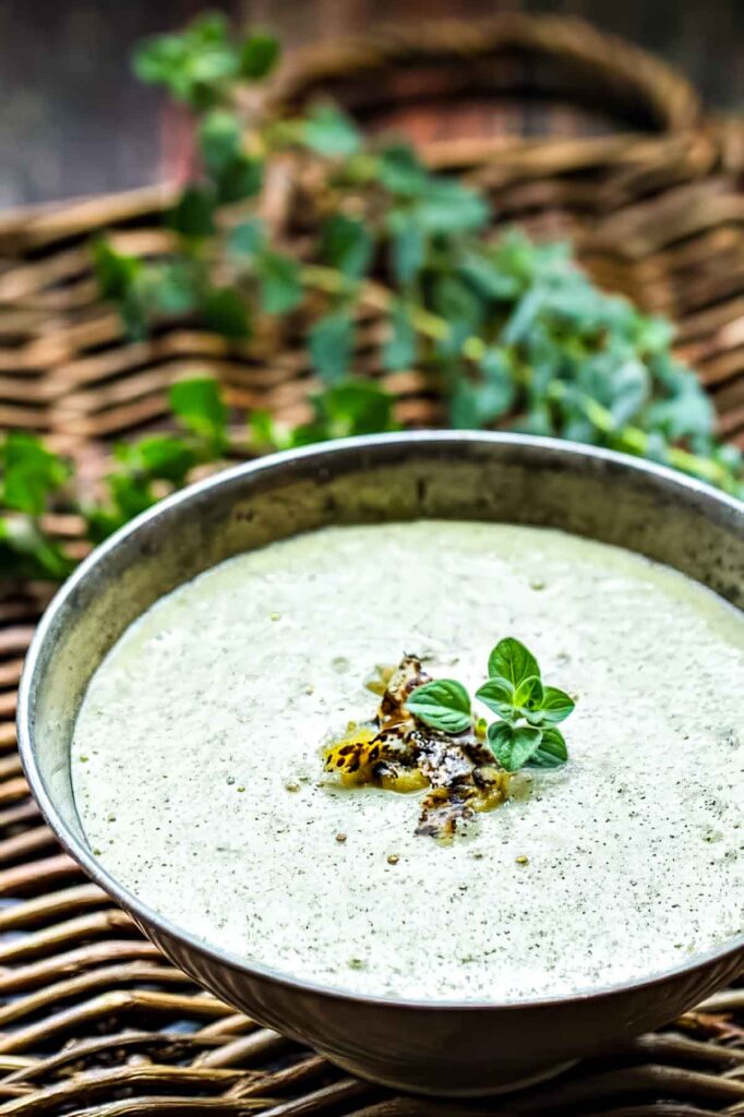 Side view of green enchilada sauce made with Hatch chiles, garnished with roasted peppers and fresh oregano in a rustic metal bowl.