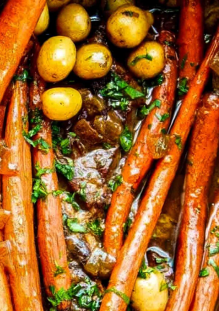 Close-up of braised carrots and baby potatoes with fresh herbs in a rich balsamic-Dijon gravy for a pot roast recipe