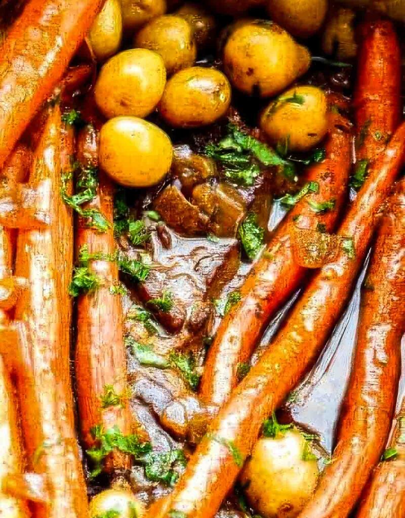 Tight close-up of glazed carrots and potatoes nestled in savory pot roast drippings as part of a chuck roast recipe