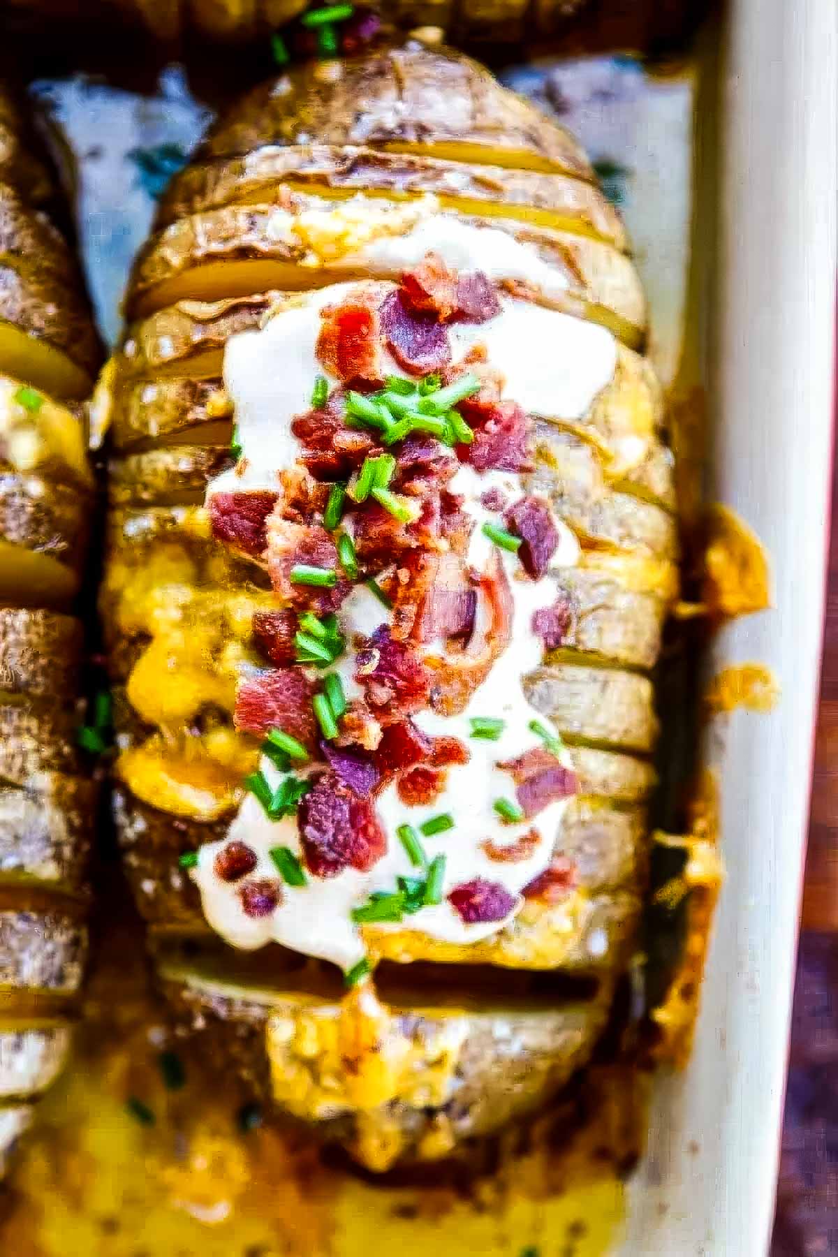 a top-down shot of a hasselback potato topped with bacon, cheese, chipotle sour cream, and chopped chives