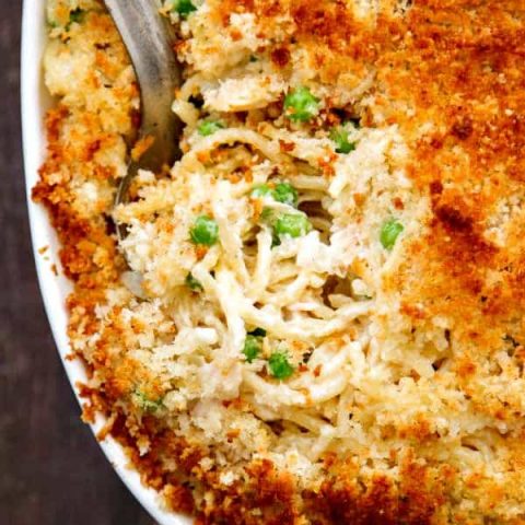 a closeup shot of turkey tetrazzini with parmesan panko topping in a white casserole dish and an antique silver spoon