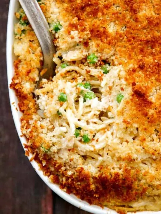 a closeup shot of turkey tetrazzini with parmesan panko topping in a white casserole dish and an antique silver spoon