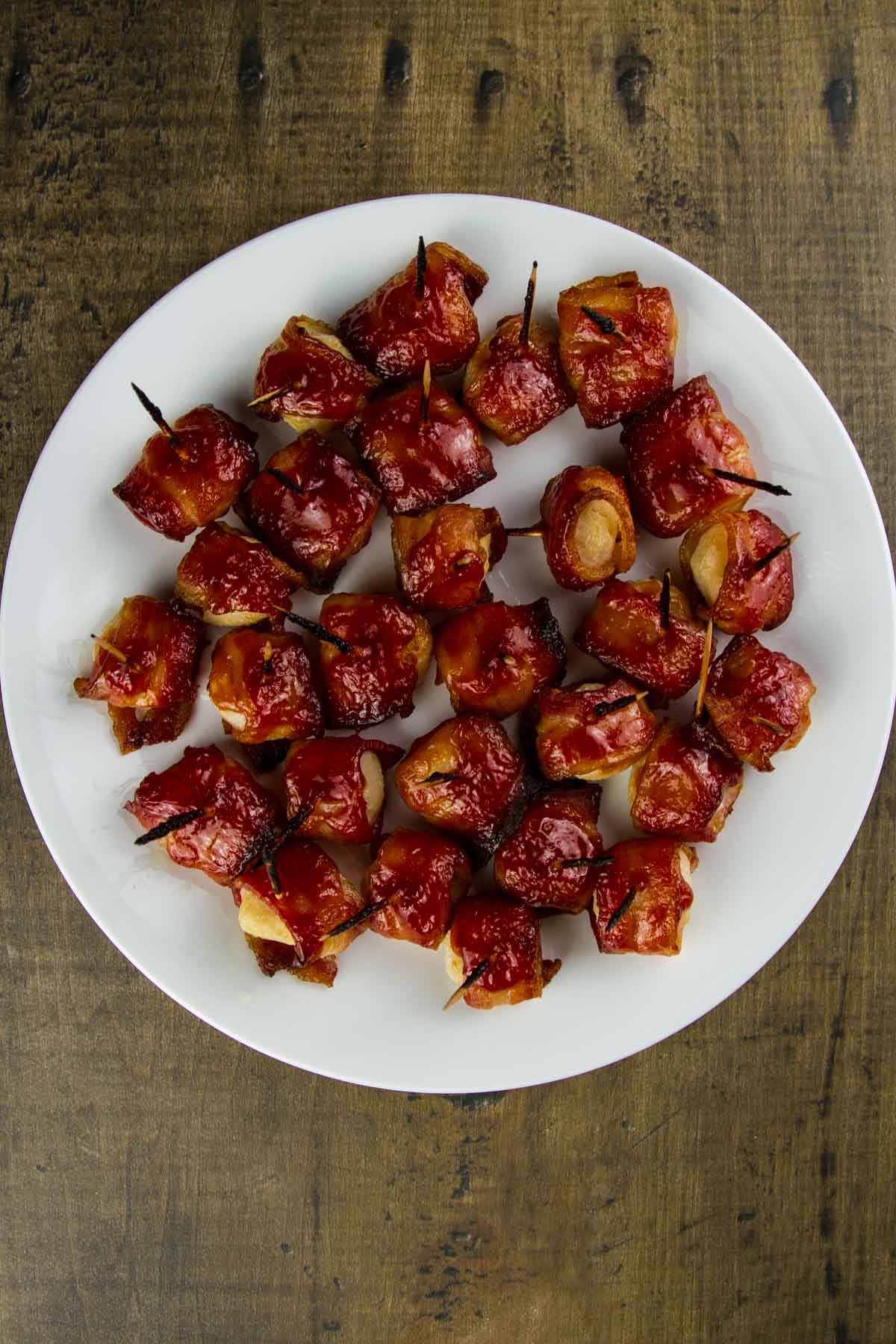 Rumaki (Bacon Wrapped Water Chestnuts) a white plate filled with rumaki (bacon wrapped water chestnuts) on a wood table