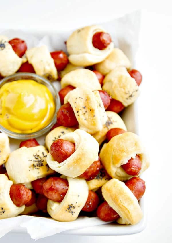 pigs in a blanket in a white bowl with a small dish of mustard