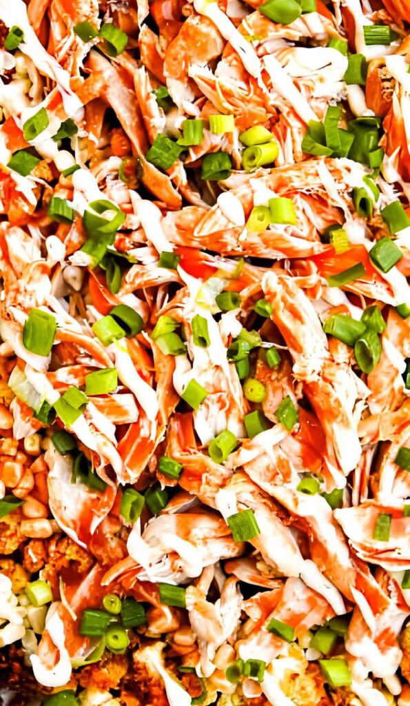 Close-up of crispy roasted cauliflower topped with shredded chicken, drizzled buffalo and ranch sauce, sweet corn, and green onions.