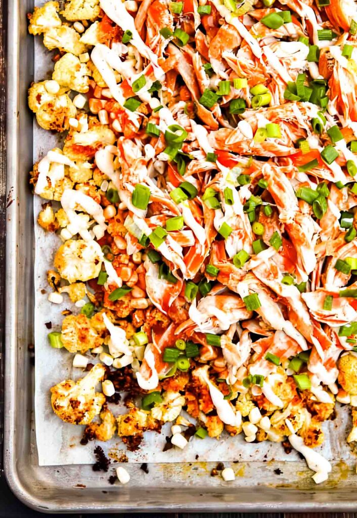 Overhead view of cauliflower nachos layered with spicy buffalo chicken, creamy ranch, fresh corn, and green onion slices.