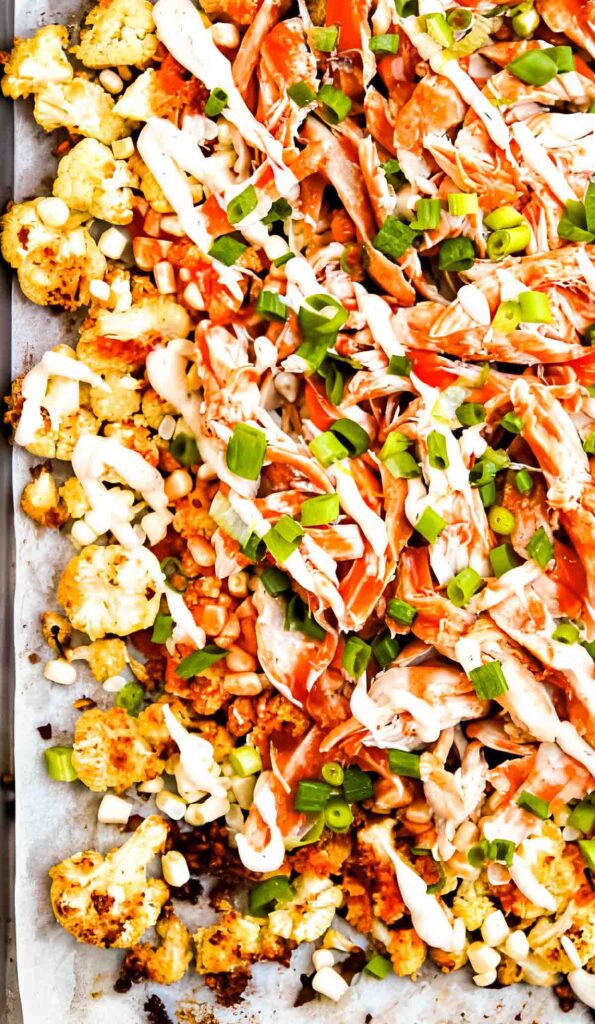 Colorful sheet pan nachos made with roasted cauliflower, shredded rotisserie chicken, tangy buffalo sauce, ranch dressing, and fresh veggies.