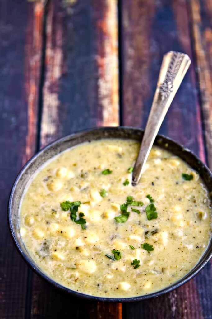 Creamy Hatch Chile Soup with Corn & Queso Fresco a bowl of hatch chile soup garnished with chopped parsley on a rustic wooden table