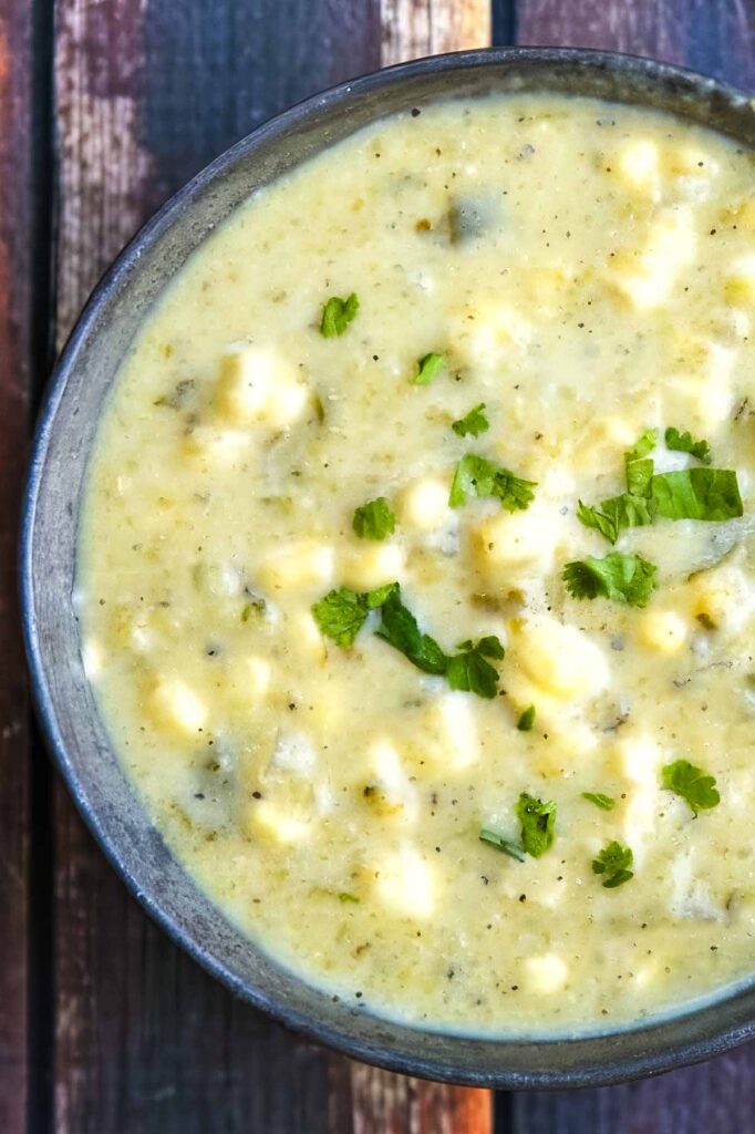 a closeup overhead shot of a bowl of hatch chile soup garnished with chopped parsley on a rustic wooden table