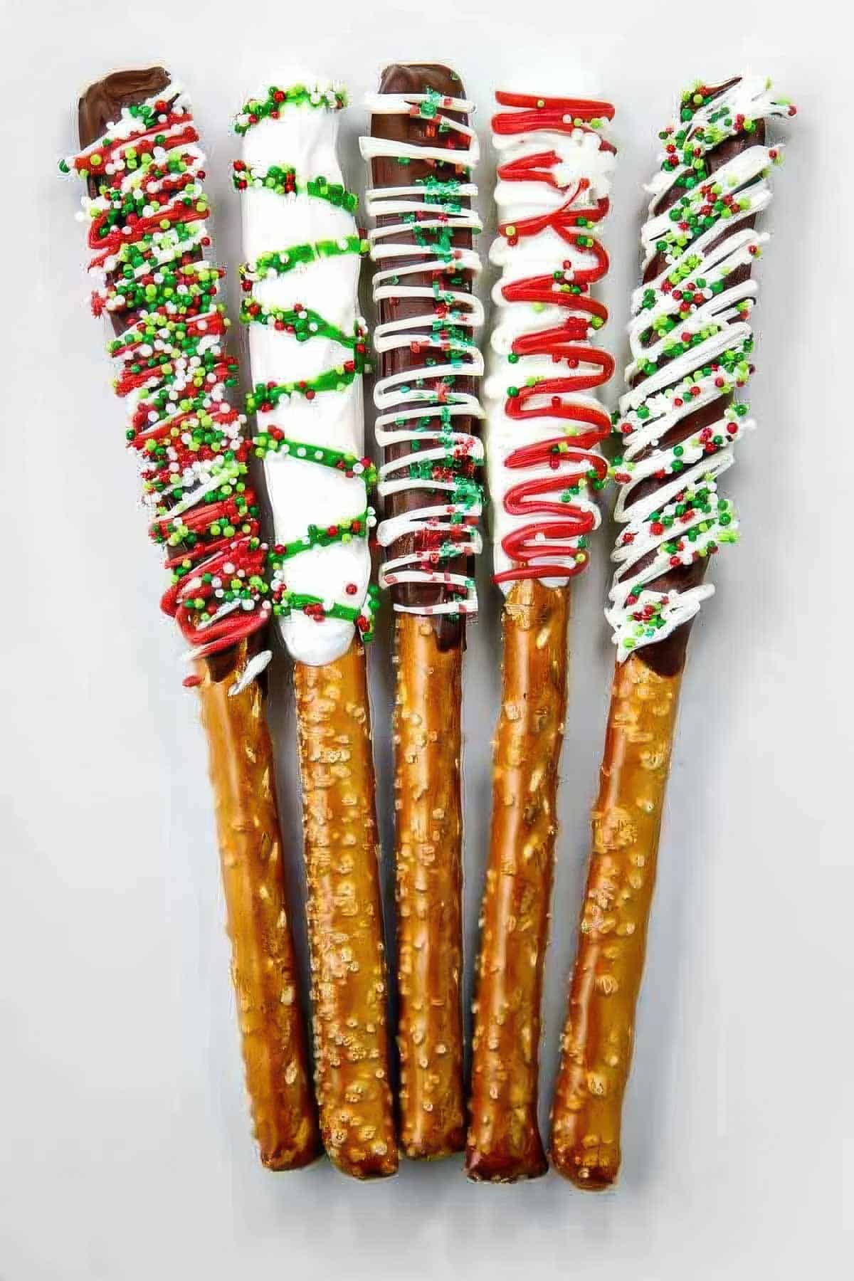 Five chocolate covered pretzel rods decorated with different colors and sprinkles for Christmas