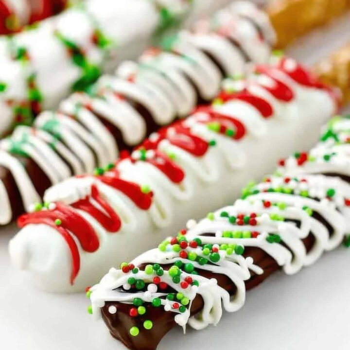 A side view of five chocolate covered pretzel rods decorated with different colors and sprinkles for Christmas