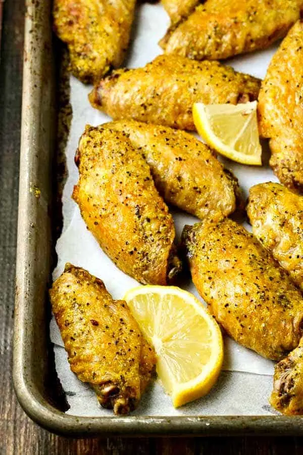 Lemon pepper wings just out of the oven with slices of lemon wedges on a sheet pan lined with parchment paper