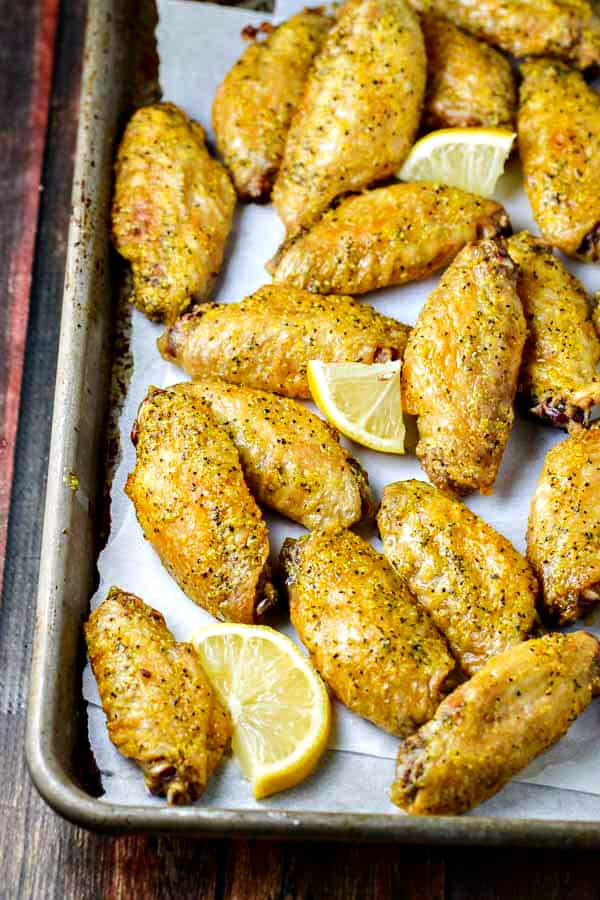 Baked lemon pepper chicken wings just out of the oven with slices of lemon wedges on a sheet pan lined with parchment paper