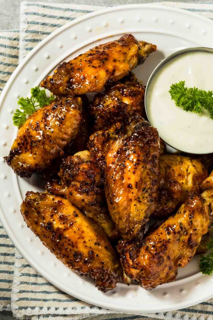 a platter of hot honey chicken wings with a small dish of ranch dressing for dipping
