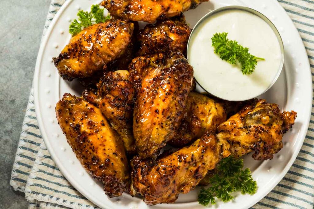 a platter of oven-baked hot honey chicken wings with a small dish of ranch dressing for dipping