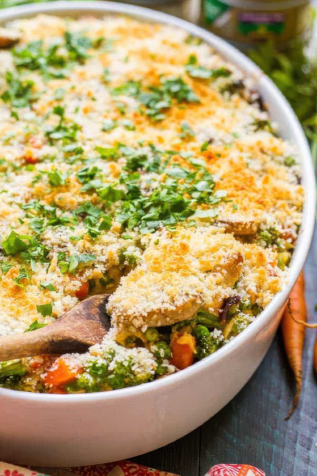 Healthy Tuna Noodle Casserole a healthy tuna noodle casserole in a white, oval baking dish with a spoon scooping out the first serving