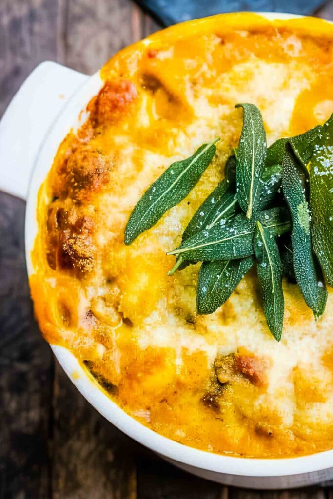 Close-up of the golden cheesy top layer of baked pumpkin gnocchi with crispy sage leaves and bubbling edges.