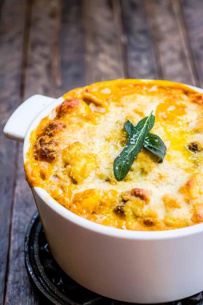 Side view of cheesy baked pumpkin gnocchi in a white baking dish, garnished with fried sage leaves.